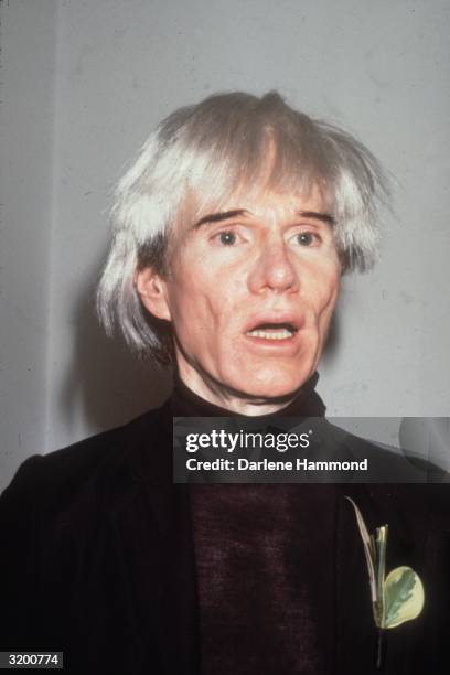 American artist Andy Warhol talking, wearing a black jacket and a turtleneck with a leaf brooch.