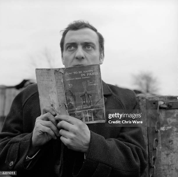 Harry H Corbett looks up from a tattered book called 'How To Be Happy In Paris' in his role as Harold Steptoe, a rag-and-bone man of frustrated...