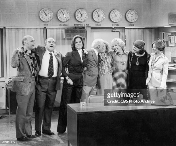 The cast of 'The Mary Tyler Moore Show' stands with their arms around each other in the newsroom in a promotional portrait for the series finale....