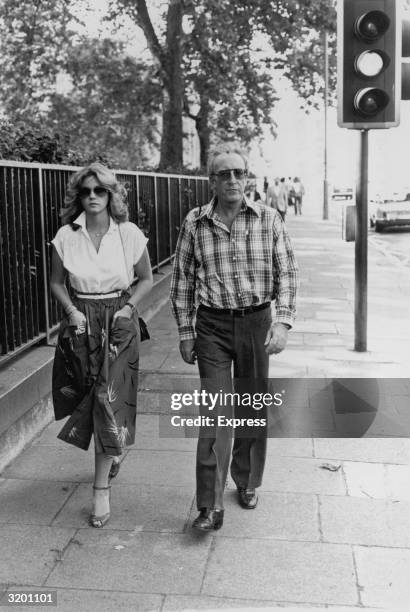 Full-length image of British actor and comedian Peter Sellers and his wife, British actor Lynne Frederick, walking down the street in London, England.