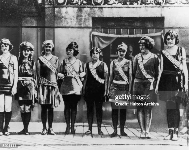 Full-length portrait of the first Miss America contestants, wearing their sashes over swimsuits, standing in a line on the boardwalk in Atlantic...