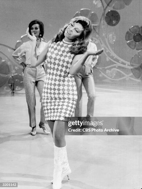 American singer Nancy Sinatra performs on stage, with backup dancers and a floral backdrop, in a full-length still from the TV program, 'The Ed...