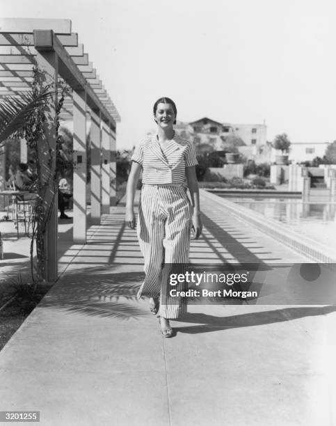 Full-length image of actor Sandra Shaw , smiling while walking on the deck of a swimming pool in a striped jacket and matching trousers at the...