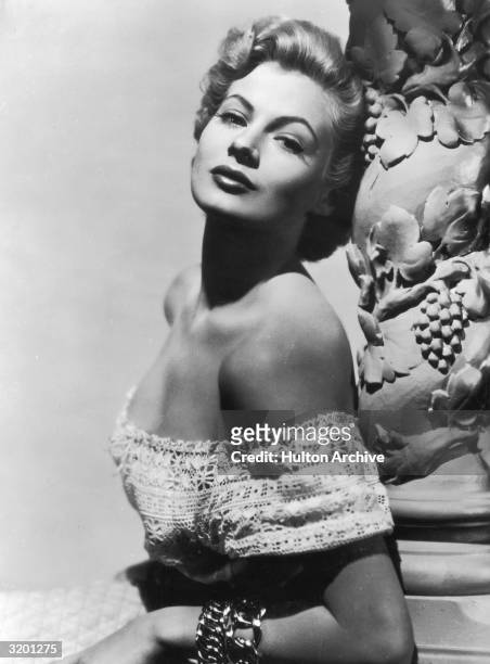 Glamour portrait of Swedish actor Anita Ekberg, wearing an off-the-shoulder dress, leaning against a column with a grapevine design.