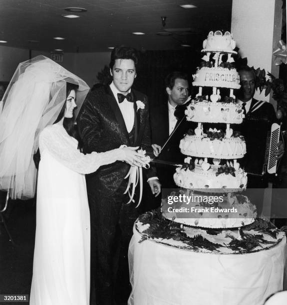 American rock n' roll singer Elvis Presley cuts his wedding cake with his wife, Priscilla Beaulieu Presley, at their wedding reception, Las Vegas,...