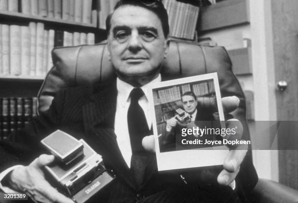 Portrait of Dr. H. Edwin Land, President and Director of the Polaroid Corporation, holding a portrait of himself posing with the Sx-70 Polaroid...