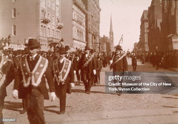 Men march in the Saint Patrick's Day Parade, wearing Irish sashes and carrying banners, in midtown Manhattan, New York City, Monday. The steeple of...