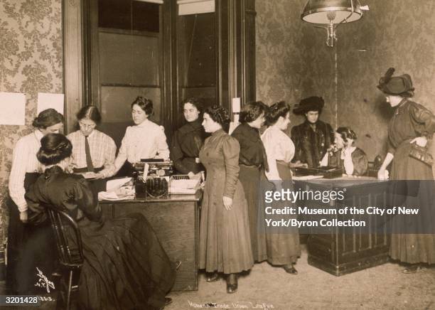 Full-length view of an all-female staff working while seated at and standing around desks in the Headquarters of the Women's Trade Union League of...