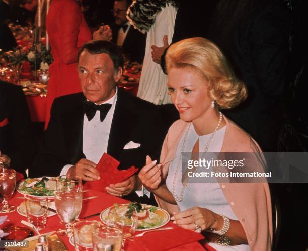 American actor and singer Frank Sinatra sitting at a dinner table next to his fiancee, showgirl Barbara Marx, at the American Film Institute Tribute...