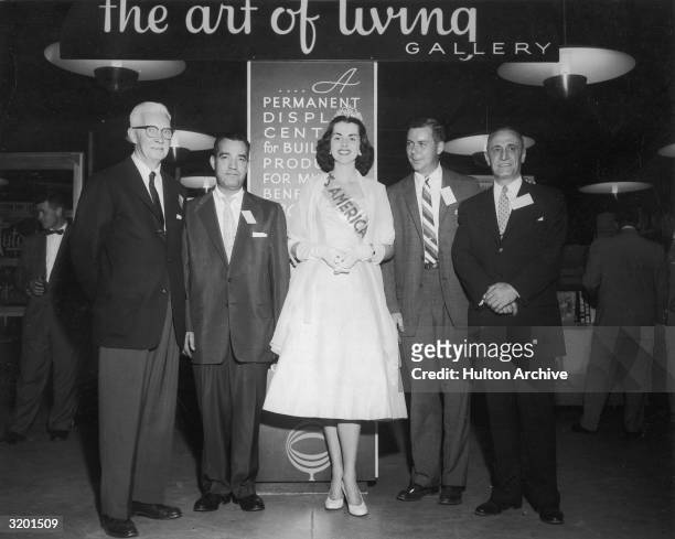 Full-length portrait of Mrs Lynwood Findley, Mrs America, smiling while posing with business executives in front of a gallery at Roosevelt Field,...