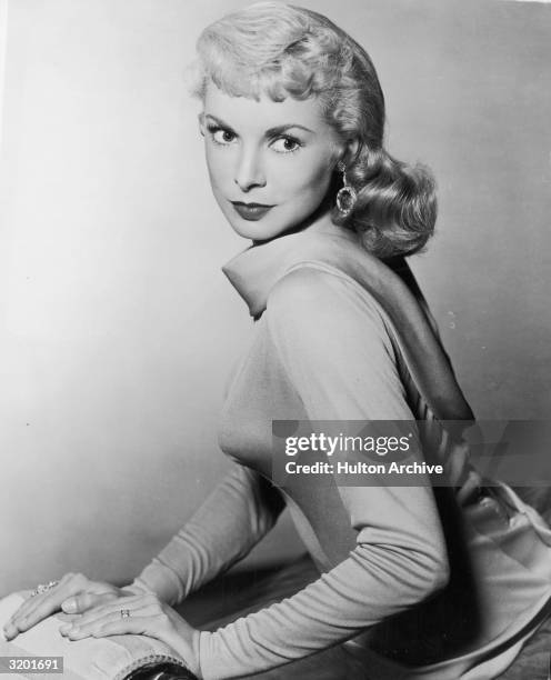 Seated portrait of actor Janet Leigh looking over her shoulder, wearing a satiny cowl neck dress.