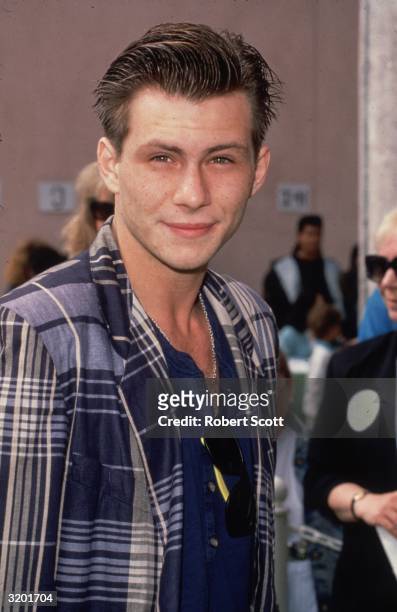 American actor Christian Slater looks into the camera at an unidentified event. He is wearing a blue plaid jacket over a blue shirt, and sunglasses...