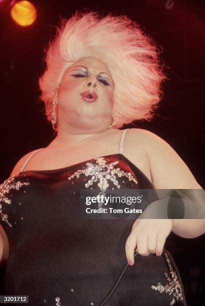 American actor and drag queen Divine performs at the Red Parrot nightclub in New York City. Divine is wearing a platinum blond wig, make-up, and a...