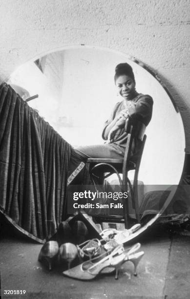 Seated portrait of American singer Nina Simone , seen reflected in a round mirror in her dressing room, at the Village Gate before a live recording...