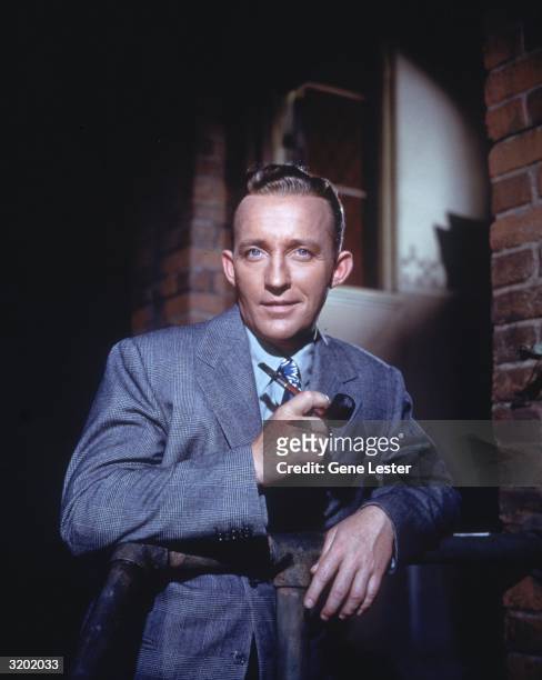 American actor and singer Bing Crosby poses for a portrait holding a pipe in his hand.