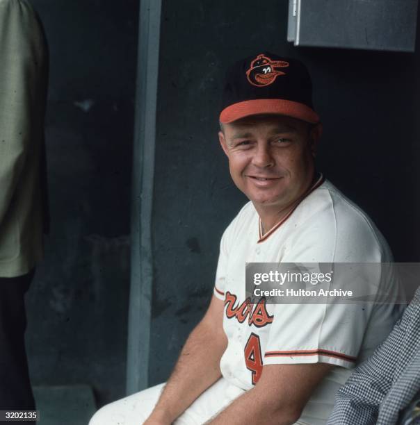Portrait of baseball manager Earl Weaver, wearing a Baltimore Orioles uniform, seated in a dugout.