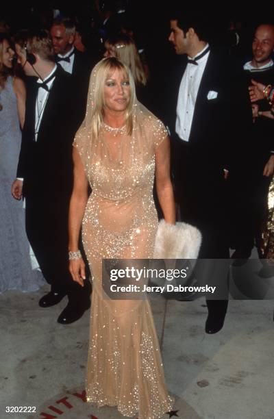 Full-length image of American actor Suzanne Somers holding a faux fur muff in a nude-colored diaphanous hooded dress with strategically placed...