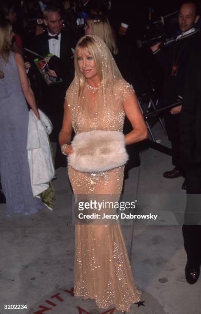 Full-length image of American actor Suzanne Somers holding a faux fur muff in a nude-colored diaphanous hooded dress with strategically placed...