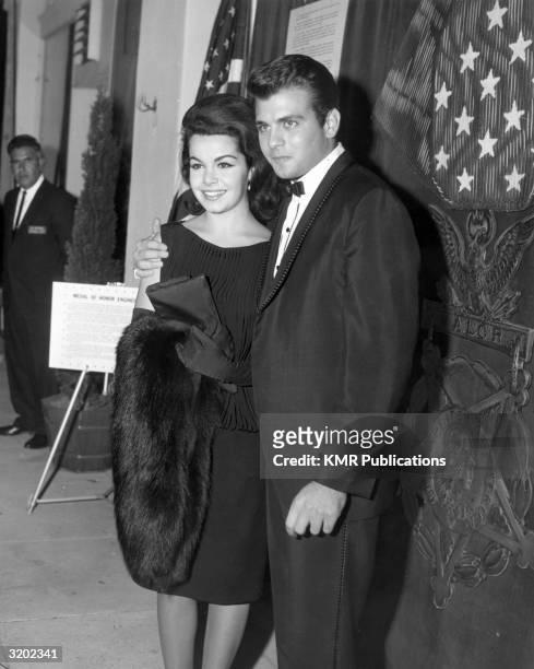 American actors and singers Annette Funicello and Fabian smile while standing with arms around each other, in front of a large-scale replica of a...
