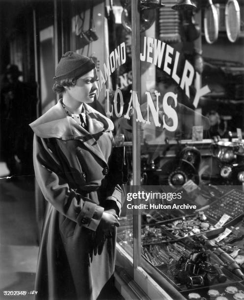 American actor Sylvia Sidney , wearing a trench coat, looks into a pawnshop window in a still from director Fritz Lang's film, 'You Only Live Once'.