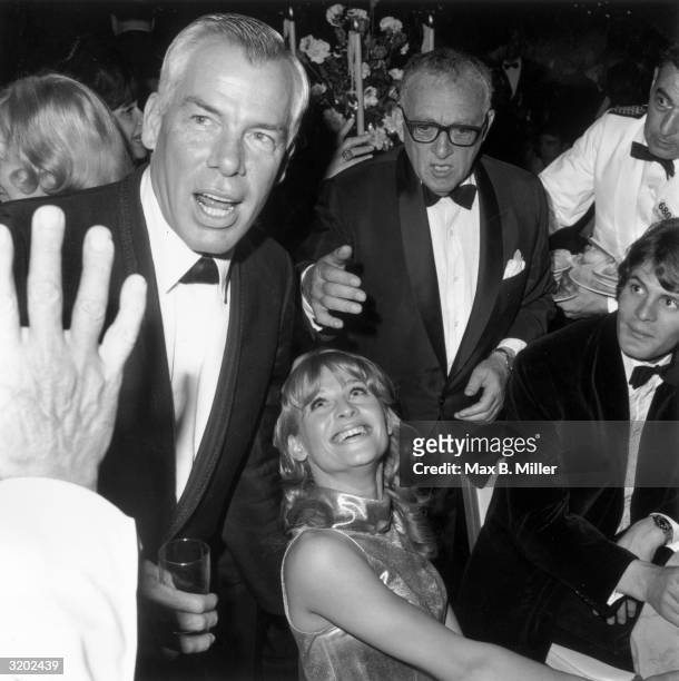 American actor Lee Marvin, holding a drink, speaks while British actor Julie Christie looks up and smiles from a table during a party for the Academy...
