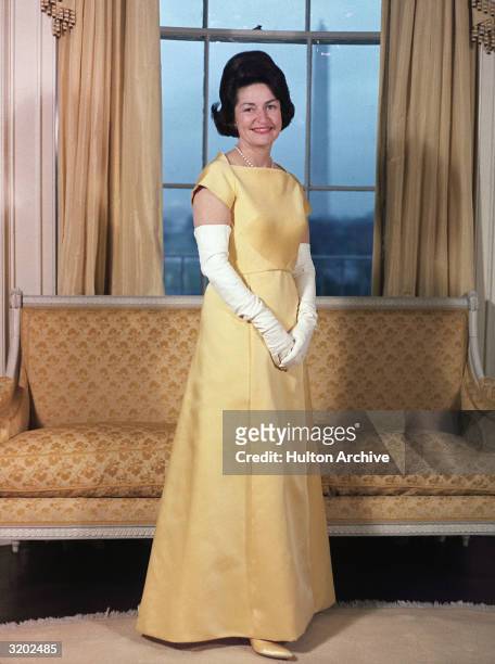 Full-length formal portrait of American First Lady Claudia 'Lady Bird' Johnson, nee Claudia Alta Taylor, wearing a yellow gown with long white...