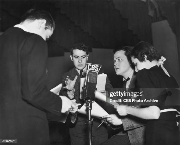 American actor and film director Orson Welles and other actors gather around a microphone while performing the radio drama 'It Might Have Happened To...