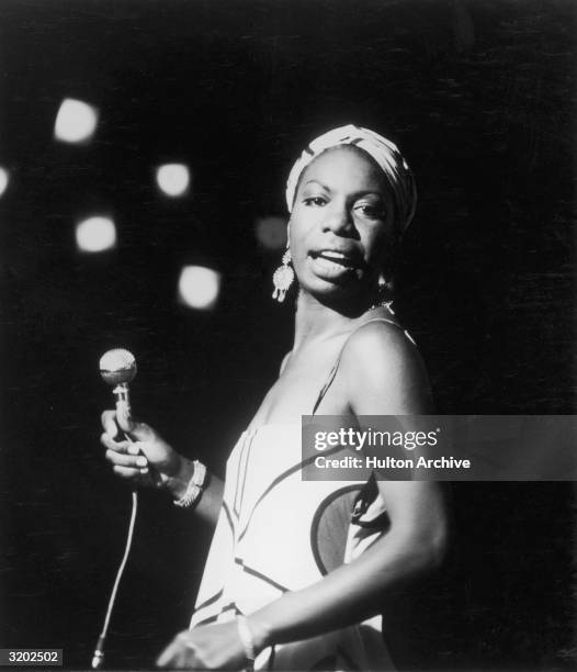 Portrait of American pianist and jazz, folk, and gospel singer Nina Simone looking over her shoulder while performing. Simone is wearing a slip dress...