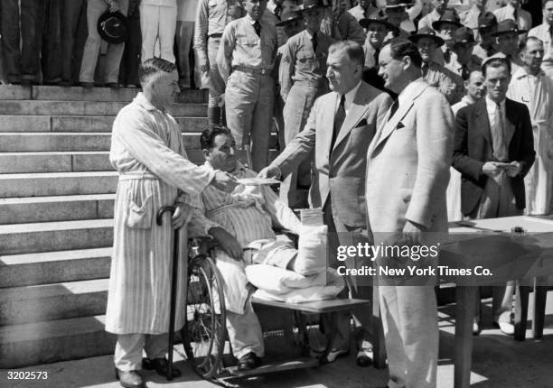 Patrick J. Ludy, of Elizabeth, New Jersey, and another veteran, seated with a cast on his leg in a wheelchair, receive bonus bonds from Postmaster...