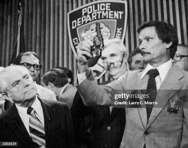 New York mayor Abraham Beame looks on as police detective Edward Zigo holds up a .44 caliber revolver, the alleged murder weapon of the 'Son of Sam'...