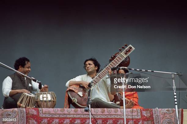 Low-angle view of Indian classical musician Ravi Shankar playing a sitar onstage with a tabla player and a string player during his performance at...