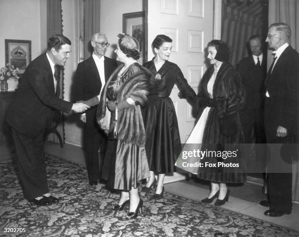 Queen Elizabeth the Queen Mother shaking hands with royal dress designer Norman Hartnell. Princess Margaret is entering the room behind her mother.