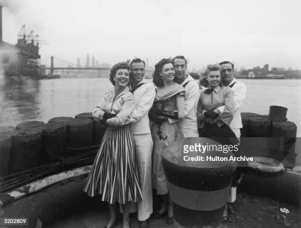 American actors Betty Garrett, Frank Sinatra, Ann Miller, Jules Munshin, Vera-Ellen and Gene Kelly smile while posing on a pier in a full-length...