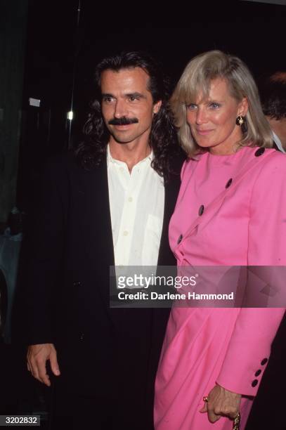 American actor Linda Evans and her boyfriend, Greek composer Yanni, smile while standing with an arm around each other at an event. Evans wears a hot...