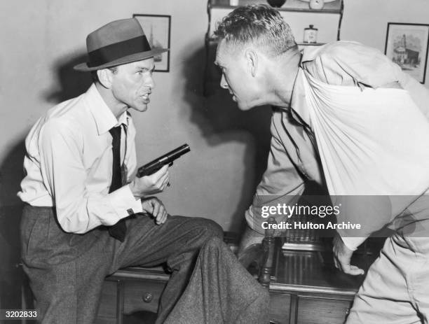 American actor and singer Frank Sinatra yells while pointing a gun at Sterling Hayden, wearing his arm in a sling, in a still from director Lewis...