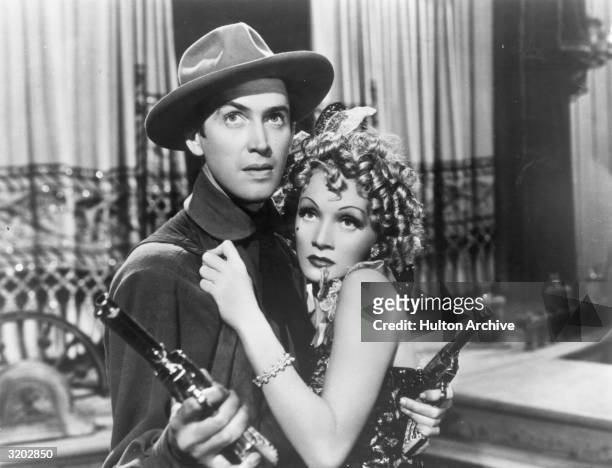 American actor James Stewart wields two pistols as German-born actor and singer Marlene Dietrich clings to him fearfully, in a still from director...