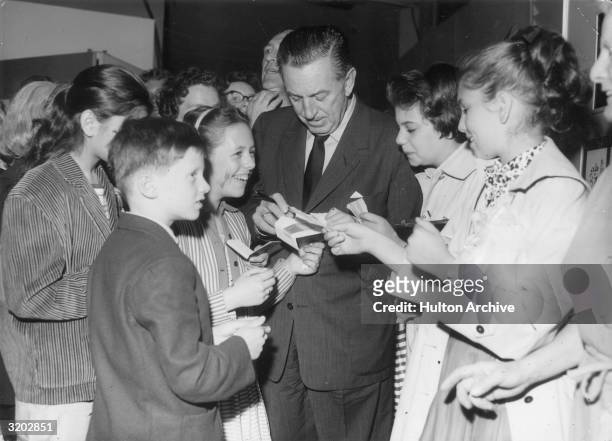 American cartoonist and producer Walt Disney signs autographs for a group of smiling young fans during the opening of the 'Art of Animation'...