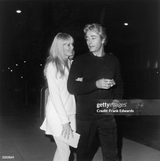 American film director and actor John Derek and his wife, American actor Linda Evans, walk together at the Daisy Club anniversary party. Derek holds...