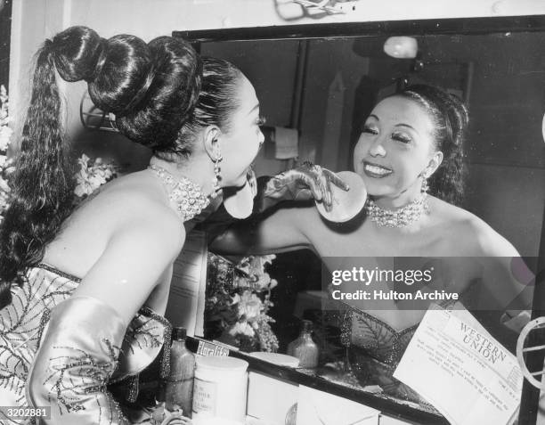 American-born cabaret singer Josephine Baker applies makeup with a powder puff in her dressing room before a performance at the Strand Theatre. A...