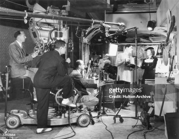 American actor William Powell plays an accordion for actor Myrna Loy while director Richard Thorpe sits on the set of his film, 'Double Wedding'. An...