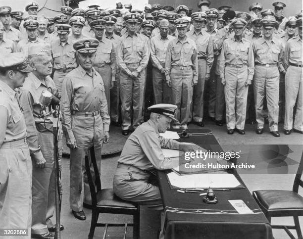 Fleet Admiral Chester W. Nimitz signs surrender documents recognizing the defeat of Japan as officials and soldiers look on, USS Missouri, Tokyo Bay,...
