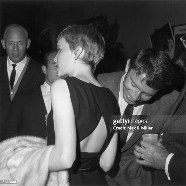 American actor Mia Farrow chats as actor Gardner McKay bends forward to look at her exposed lower back during a 20th Century Fox studio party,...