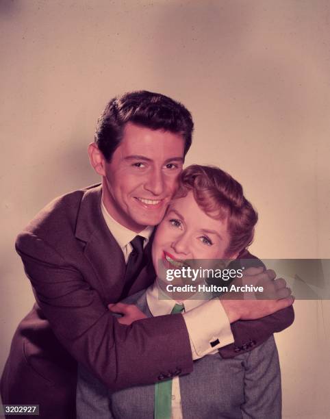 Headshot studio portrait of married American singer/actors Eddie Fisher and Debbie Reynolds; Fisher stands behind Reynolds, his arms around her...