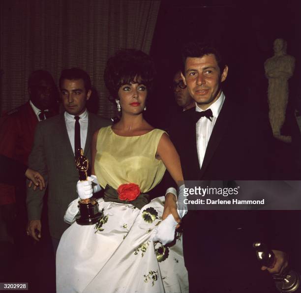 British-born actor Elizabeth Taylor, holding the Oscar she won for best actress in director Daniel Mann's film, 'Butterfield 8,' with husband,...