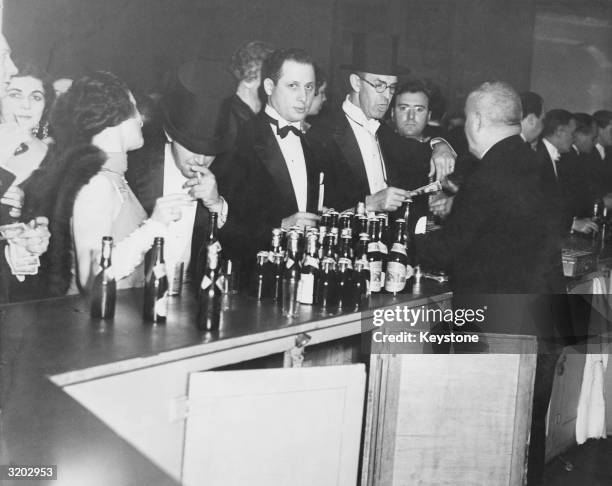 Evening dressed revellers buying their drinks at a bar at the time of prohibition.