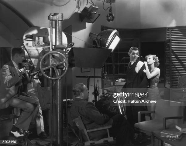 American actor Joan Crawford stands behind Clark Gable and removes his suit jacket before director Robert Z. Leonard and a camera crew, during...