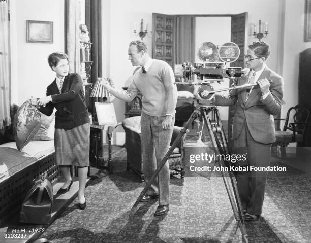 Director Sam Wood shows Canadian actress Norma Shearer how to swing a cushion on the set of 'The Latest from Paris', watched by a cameraman.