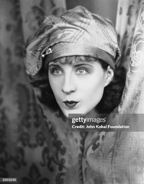 Canadian actress Norma Shearer peers through a pair of curtains in a scene from the film 'The Demi-Bride', directed by Robert Z Leonard.