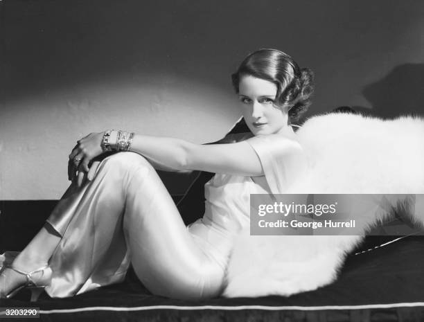 Hollywood film actress, Norma Shearer reclining in a satin dress.