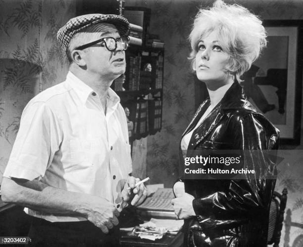Austrian-born director Billy Wilder smokes a cigarette while directing American actor Kim Novak on the set of his film, 'Kiss Me, Stupid'. Novak has...